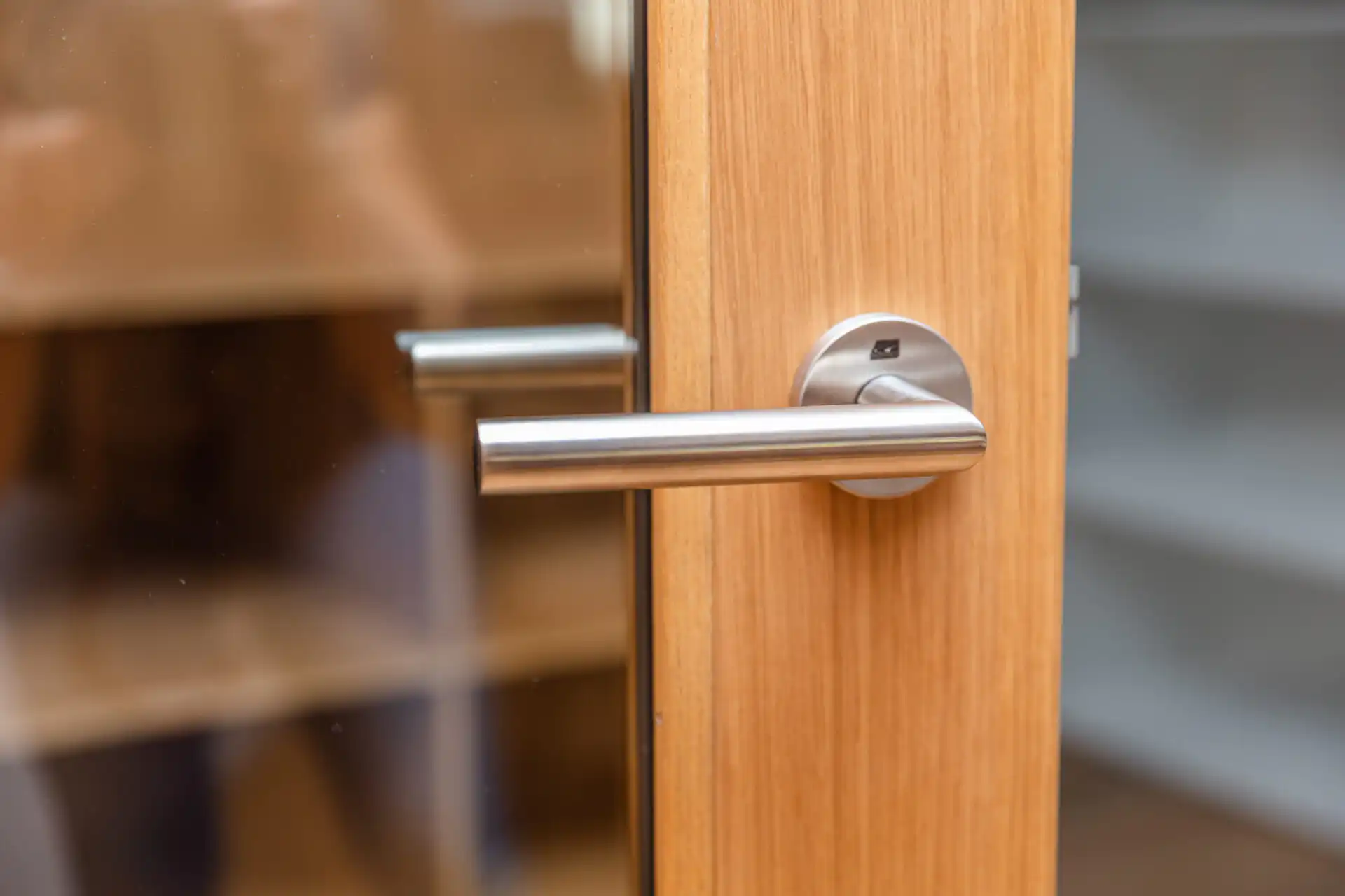 Moderner Türgriff aus Edelstahl an einer Holztür, Nahaufnahme. Ideal für stilvolle Inneneinrichtung und modernes Design.